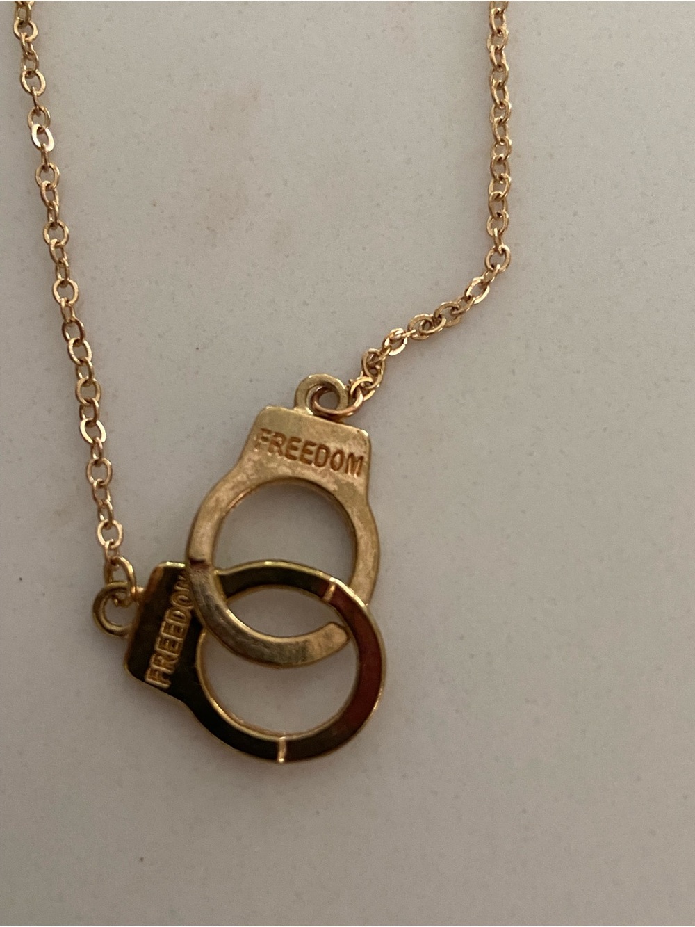 Freedom gold tone handcuff pendant necklace features two interlocking cuffs